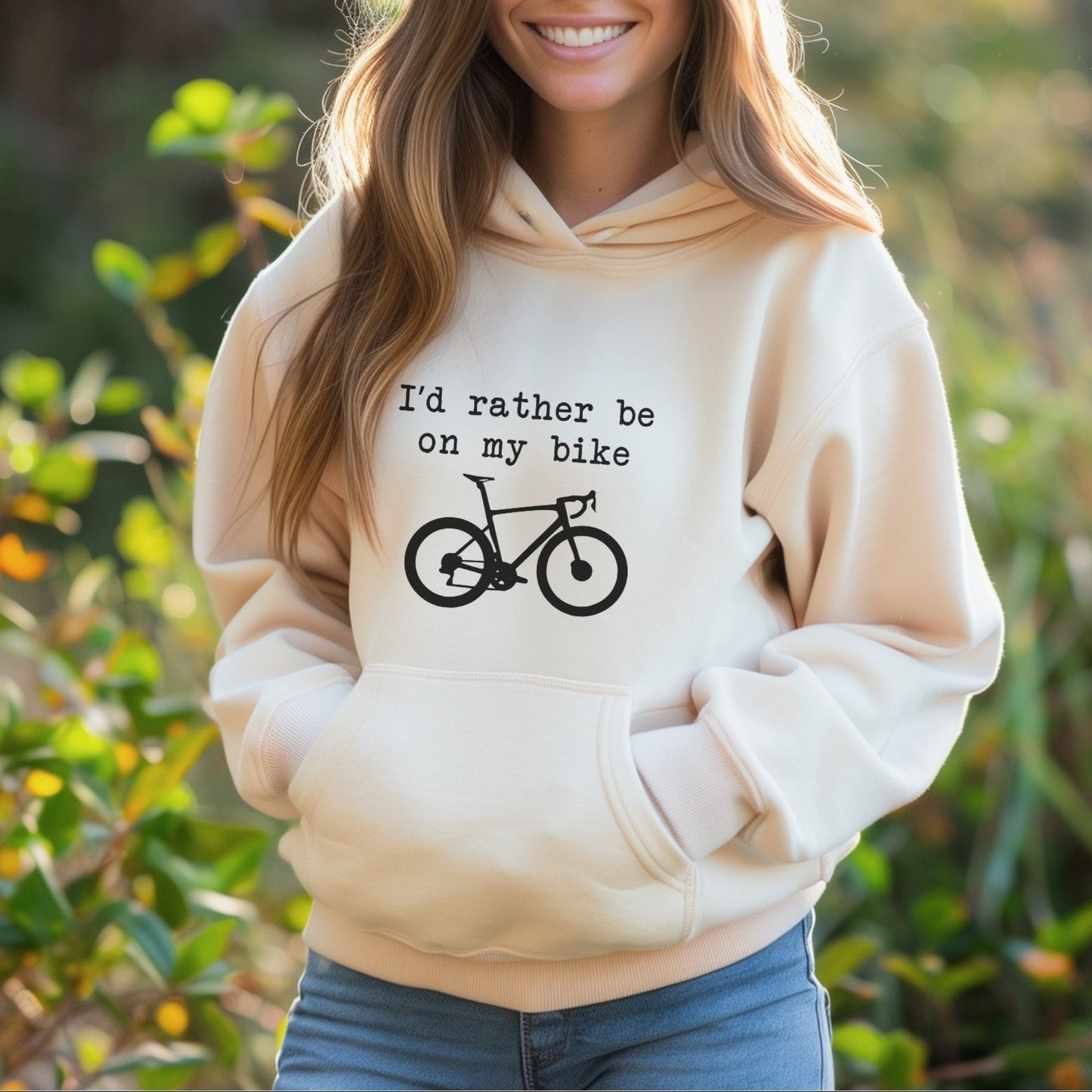 Woman wearing a beige hoodie with a bicycle graphic and text, standing outdoors.