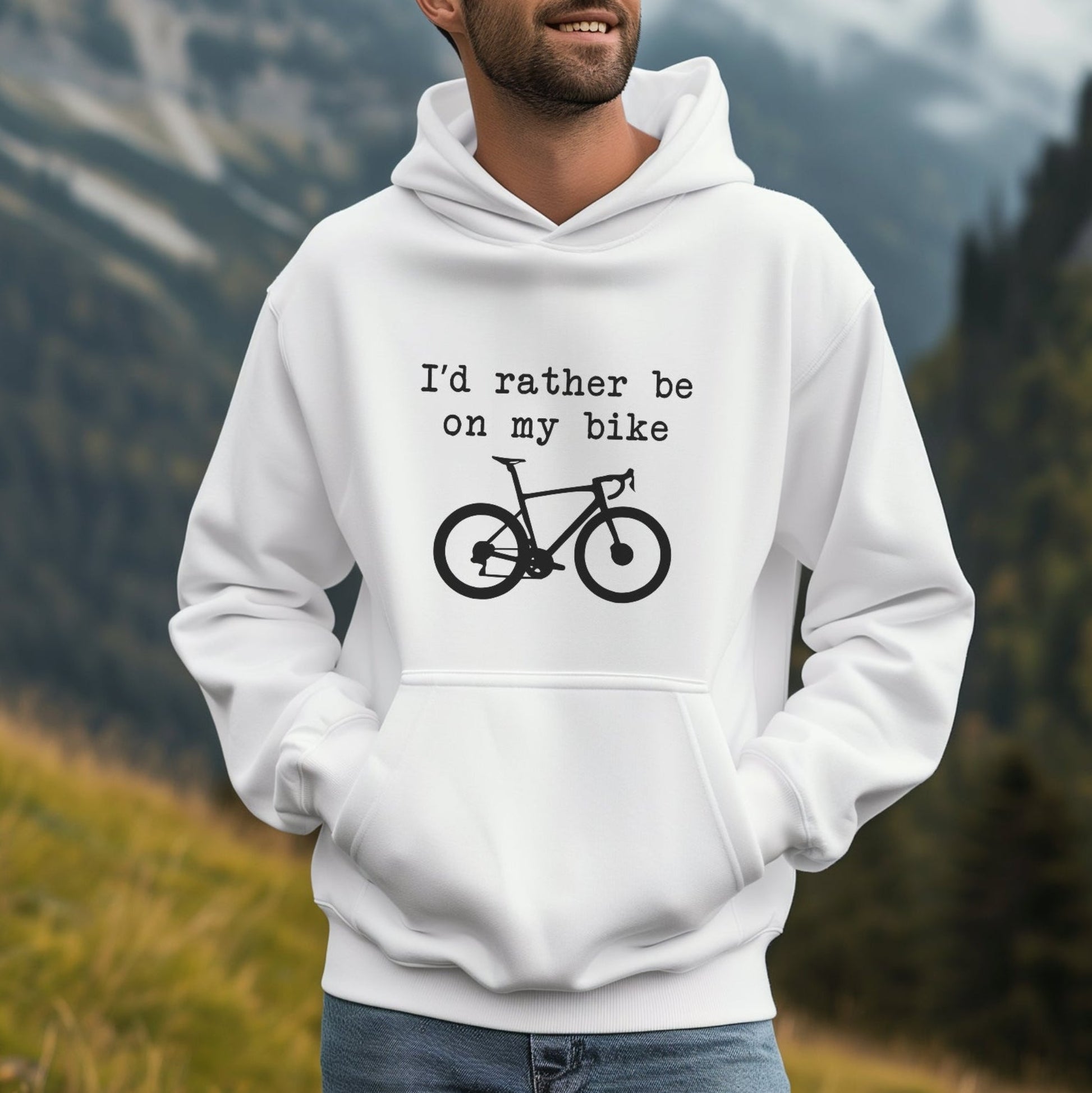 Person wearing a white hoodie with 'I'd rather be on my bike' text and bicycle graphic, standing in a mountainous area.