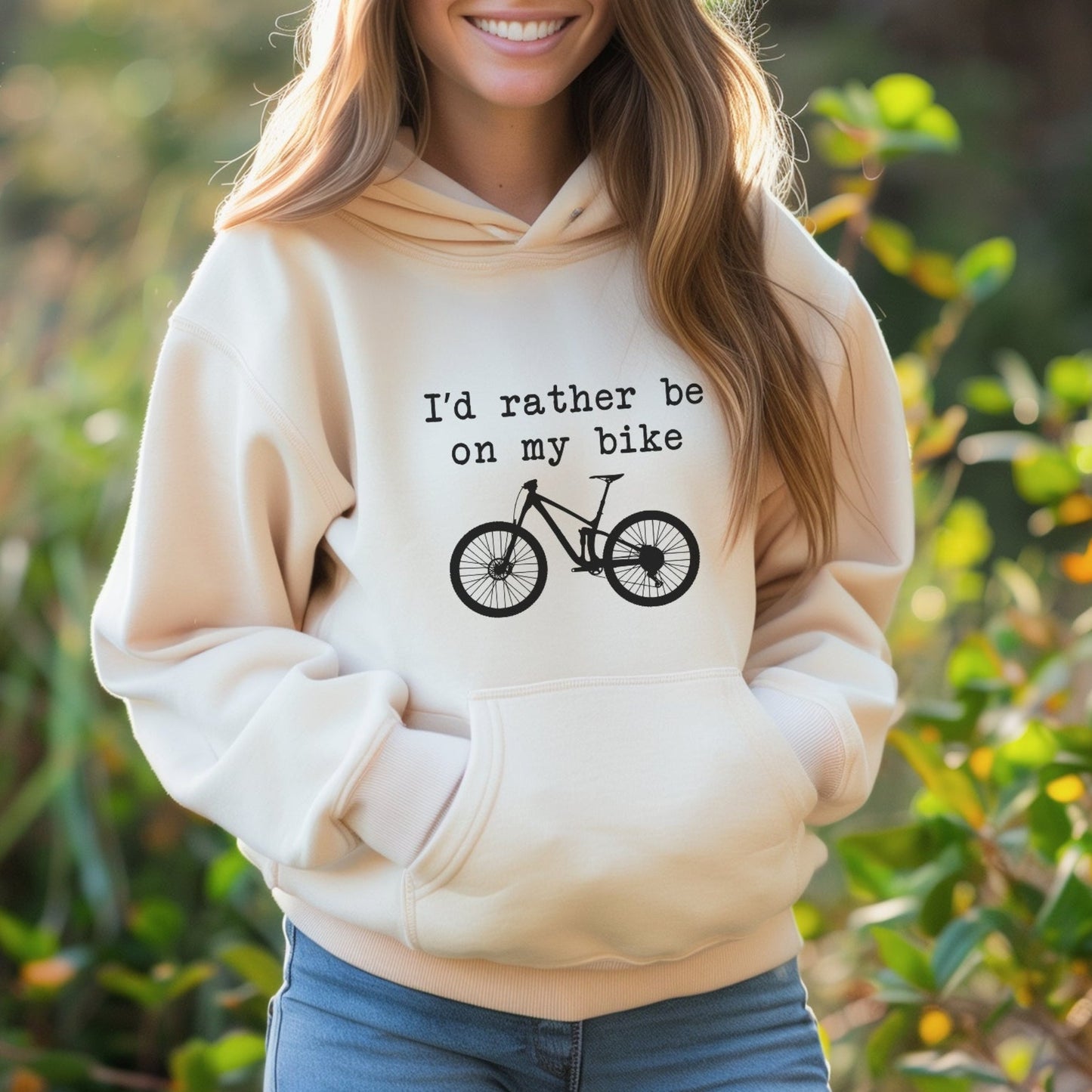 Woman wearing a beige hoodie with a bicycle graphic and text, standing outdoors.