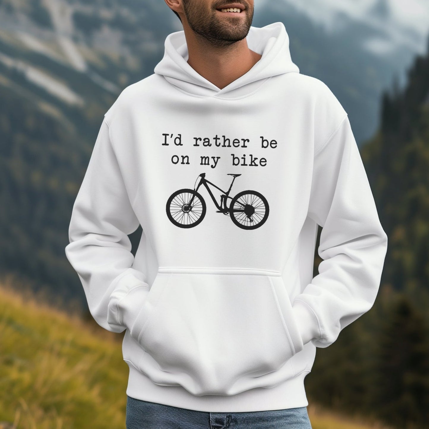 Man wearing a white hoodie with a bicycle graphic and text in a mountainous landscape