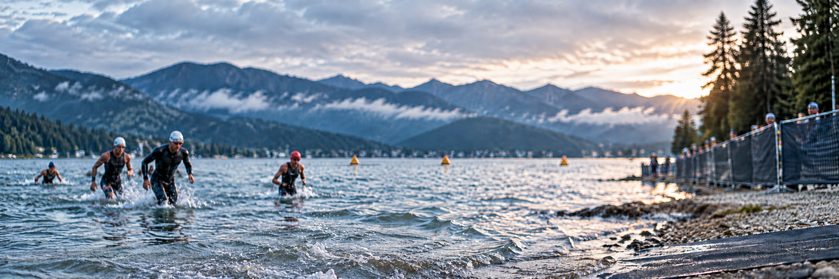 Triathletes swimming toward the exit around orange buoys on a mountain lake